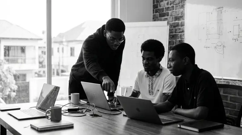 Three people working together at laptops around a table in a bright office